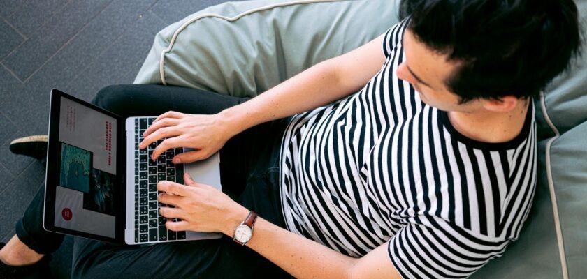 A man in a striped shirt using a laptop on a bean bag, embodying relaxed productivity.